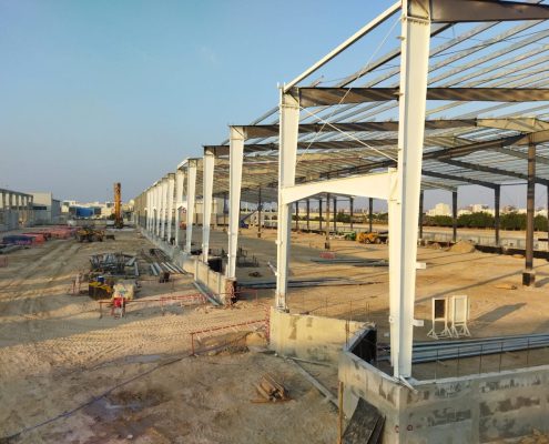 Elevated view of white steel columns and roof trusses at a large construction site