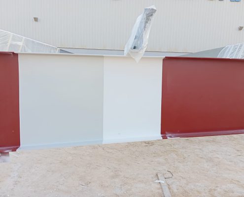 Large steel girder sections with red primer and white intumescent coating at a fabrication yard