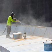 Worker in protective gear spray-applying cementitious fire protection coating to a steel tank