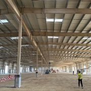 Wide interior view of an industrial warehouse under construction with steel roof trusses