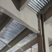 Close-up of gray cementitious fireproofing coating sprayed onto a steel beam and joist