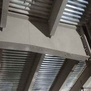 Angled close-up of gray cementitious fire protection coating on a steel beam