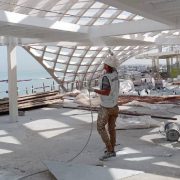 Worker spray-applying fire protection coating to a timber structure at a coastal construction site
