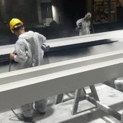 Technicians in PPE spray-applying fire retardant coating to steel beams in a Dubai workshop