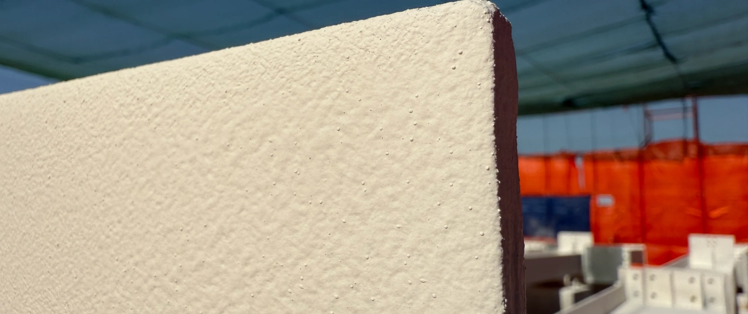 Close-up edge of a steel plate coated in cream intumescent paint on a construction site