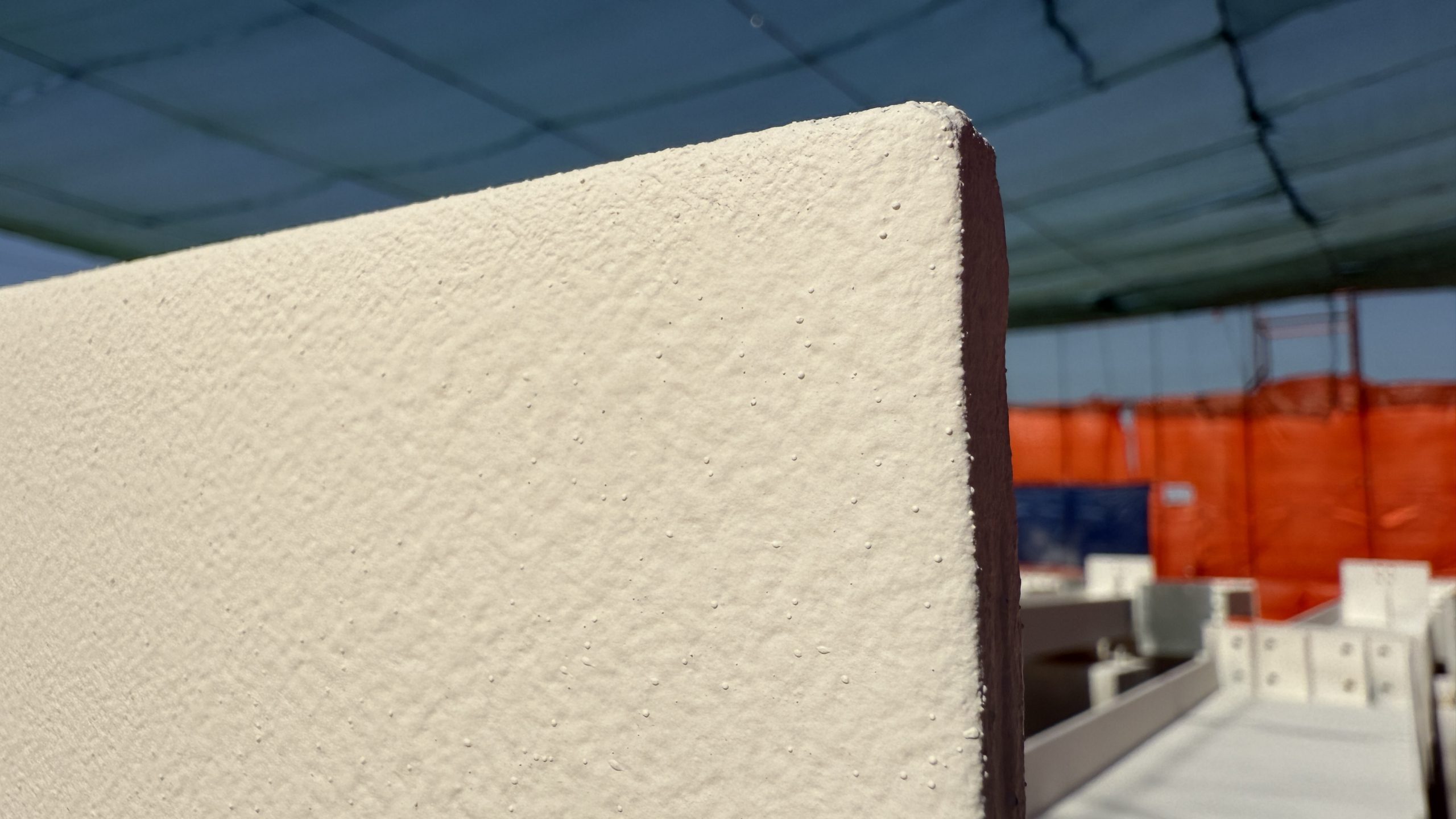 Close-up edge of a steel plate coated in cream intumescent paint on a construction site