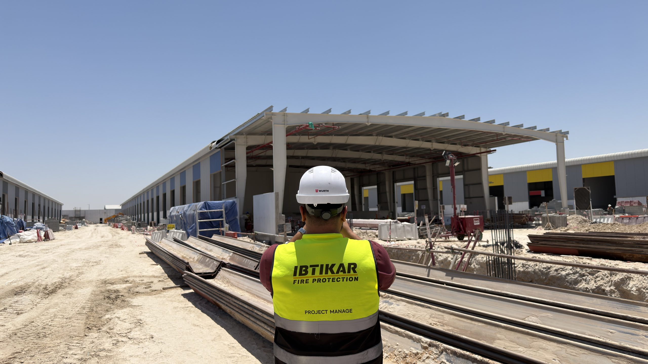 Ibtikar Fire Protection project manager in branded hi-vis vest overlooking a warehouse construction site